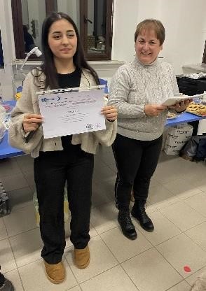 eine SchĂŒlerin hĂ€lt ein Zertifikat hoch, neben ihr steht eine Lehrkraft